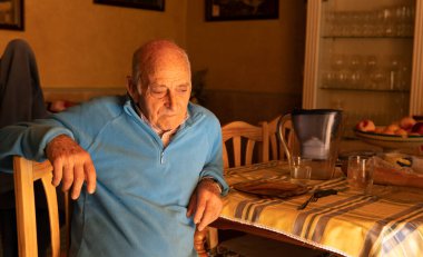 Yaşlı adam oturdu, mavi bir kazak giydi, evde yemeye hazırdı, yatay çekim.