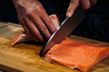 Aşçının elleri Japon bıçağıyla geleneksel Asya mutfağı için somon balığı doğruyor. Profesyonel suşi şefi Japon deniz ürünleri kesiyor somon balığı sashimi yapıyor. koyu ton