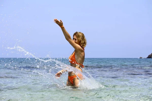 Woman throws water in the sea, splashes.