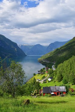 Etkileyici dağlar fiyort manzarası, kırmızı evler ve göl kenarındaki dolambaçlı yol, Aurlandsfjord Norveç