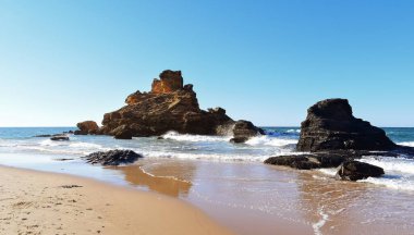 Okyanus dalgaları sahildeki kayalara çarpıyor Praia do Castelo, Algarve, Portekiz, Avrupa
