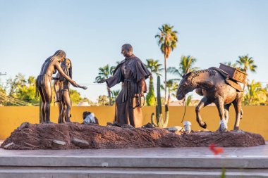 Loreto, Baja California Sur, Meksika. 17 Kasım 2021. Katolik bir rahibin heykeli yerli Meksikalılarla etkileşime geçiyor..