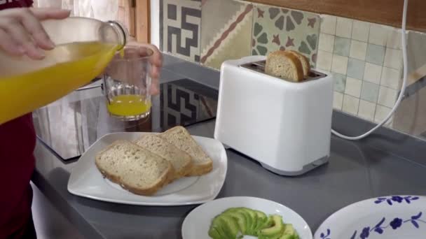 トーストとキッチンで自家製朝食のクローズアップシーン アボカドとオレンジジュース 本人は特定されていない 高品質4K映像 — ストック動画