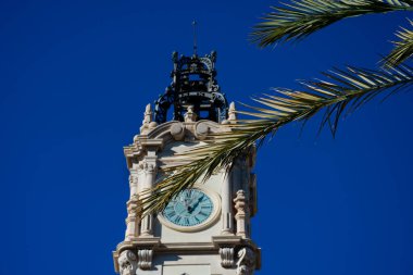 Belediye binası ağaç dallarının arkasındaki saat kulesi (Edificio del Ayuntamiento). Valencia, İspanya