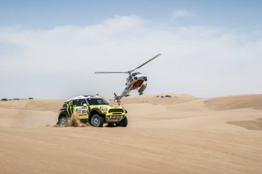 Dakar rallisinde Peru çölünde helikopterli bir yarış arabası görüntüsü.