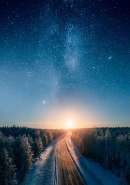 Gün batımına doğru giden yol ve karlı Boreal Ormanı 'ndan geçen Samanyolu yıldızları. Ulaşım ve İskandinav destansı manzaraları.