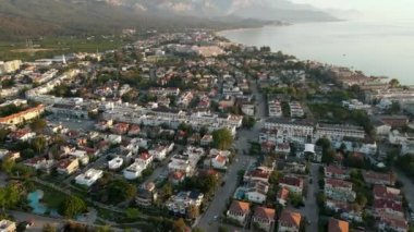 Şafakta dağlarla ve denizle çevrili bir şehrin üzerinde insansız hava aracı, hafif sis, yaz günü 4k