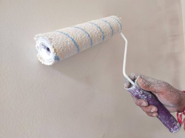 Bir ressam odada boya silindirli bir duvar boyuyor. Daire boyama, beyaz boyayla yenileme.