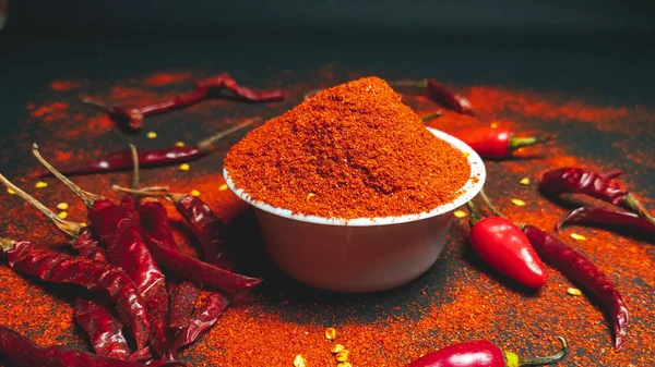 Red chili pepperand chili powder on a dark background.