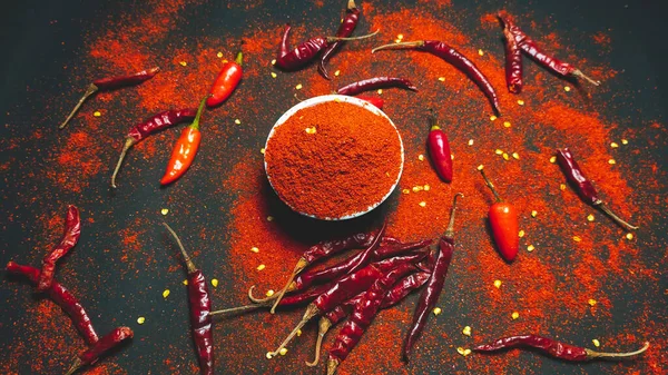 Red chili pepperand chili powder on a dark background.