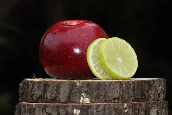 Red apple and lemon slices on big tree trunk slice