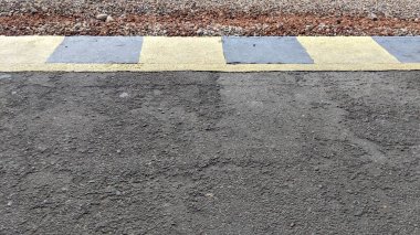 Zemin asfaltla kaplanmış ve kenarları siyaha ve sarıya boyanmış..