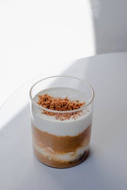 Krem şantili bir bardak kahvenin ve beyaz masanın üzerine serpiştirilmiş ezilmiş gofretin göz hizasında görüntüsü.