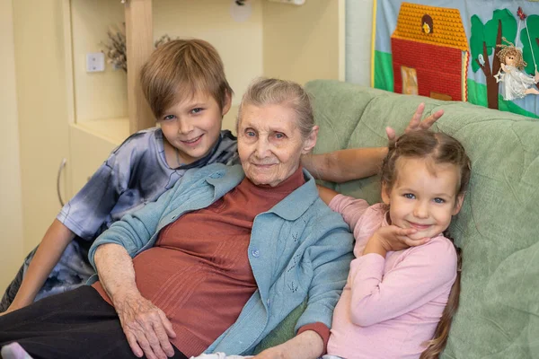 Mutlu bir aile - torunları olan bir büyükanne, bir kız ve bir oğlan büyükannelerine sarılıyorlar, hep birlikte odadaki kanepede oturuyorlar, aile bağları, çocukluk, gençlik ve yaşlılık..