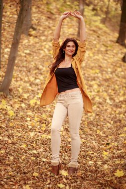 Güzel genç bir kadın ormanda bir patika boyunca yürür, sonbahar kuru yaprakları yere dökülür, yaprak düşer, Kasım.