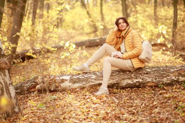 Güzel genç bir kadın ormanda bir patika boyunca yürür, sonbahar kuru yaprakları yere dökülür, yaprak düşer, Kasım.