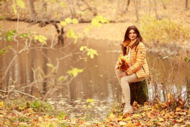 Güzel genç bir kadın ormanda bir patika boyunca yürür, sonbahar kuru yaprakları yere dökülür, yaprak düşer, Kasım.
