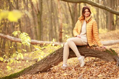 Güzel genç bir kadın ormanda bir patika boyunca yürür, sonbahar kuru yaprakları yere dökülür, yaprak düşer, Kasım.