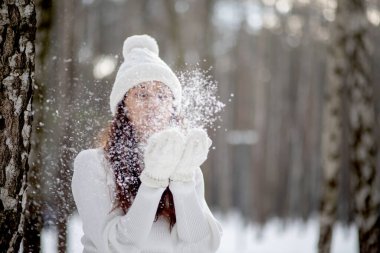Kışın parkta güzel bir genç kadın avuçlarında karlara eser, güzel kar taneleri eldivenlerinden uçar, kış havası, yeni yıl ve Noel..