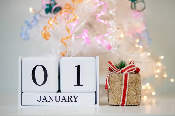 1 Ocak 'ta bir masa takvimi, oyuncak bir hediye ve beyaz arka planda yeni yıl ışıkları, güzel bir Noel geçmişi..