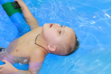 Down sendromlu bir çocuk havuzda yüzmeyi öğrenir..