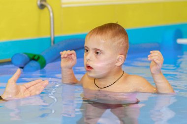 Down sendromlu bir çocuk havuzda yüzmeyi öğrenir..