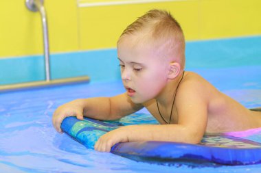 Down sendromlu bir çocuk havuzda yüzmeyi öğrenir..