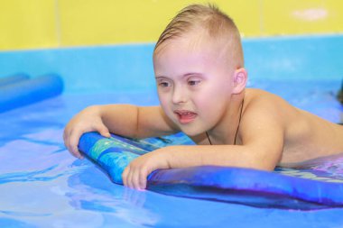 Down sendromlu bir çocuk havuzda yüzmeyi öğrenir..