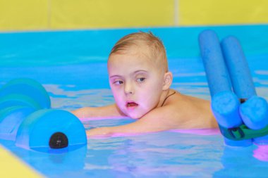 Down sendromlu bir çocuk havuzda yüzmeyi öğrenir..