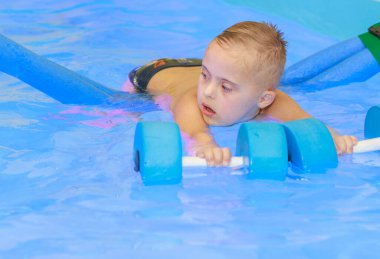 Down sendromlu bir çocuk havuzda yüzmeyi öğrenir..