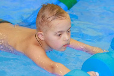 Down sendromlu bir çocuk havuzda yüzmeyi öğrenir..