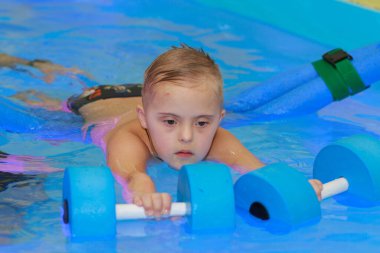 Down sendromlu bir çocuk havuzda yüzmeyi öğrenir..