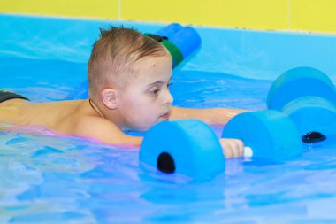 Down sendromlu bir çocuk havuzda yüzmeyi öğrenir..