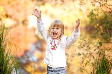 Sonbahar parkında bir kızın portresi, çocuğun etrafında parlak turuncu ve kırmızı yapraklar..