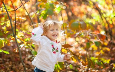 Sonbahar parkında bir kızın portresi, çocuğun etrafında parlak turuncu ve kırmızı yapraklar..