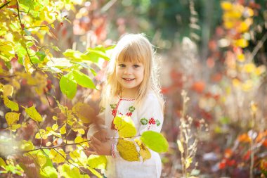 Sonbahar parkında bir kızın portresi, çocuğun etrafında parlak turuncu ve kırmızı yapraklar..