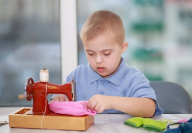 Down sendromlu bir çocuk oyuncak bebekler için elbise dikiyor, tip 21 trisonomisi olan özürlü bir çocuk, fazladan bir kromozom, özel bir çocuk..