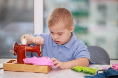 Down sendromlu bir çocuk oyuncak bebekler için elbise dikiyor, tip 21 trisonomisi olan özürlü bir çocuk, fazladan bir kromozom, özel bir çocuk..