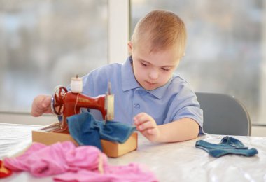 Down sendromlu bir çocuk oyuncak bebekler için elbise dikiyor, tip 21 trisonomisi olan özürlü bir çocuk, fazladan bir kromozom, özel bir çocuk..