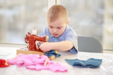 Down sendromlu bir çocuk oyuncak bebekler için elbise dikiyor, tip 21 trisonomisi olan özürlü bir çocuk, fazladan bir kromozom, özel bir çocuk..
