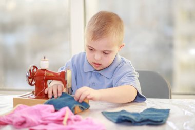 Down sendromlu bir çocuk oyuncak bebekler için elbise dikiyor, tip 21 trisonomisi olan özürlü bir çocuk, fazladan bir kromozom, özel bir çocuk..
