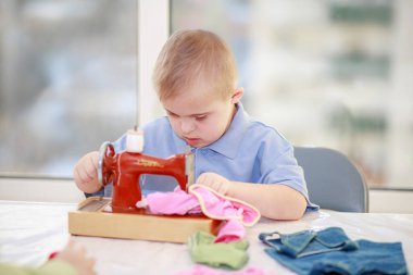 Down sendromlu bir çocuk oyuncak bebekler için elbise dikiyor, tip 21 trisonomisi olan özürlü bir çocuk, fazladan bir kromozom, özel bir çocuk..