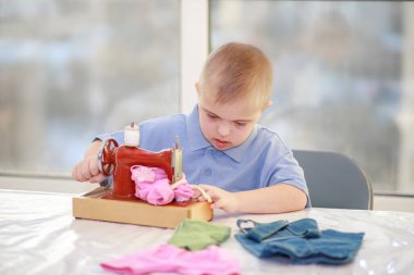 Down sendromlu bir çocuk oyuncak bebekler için elbise dikiyor, tip 21 trisonomisi olan özürlü bir çocuk, fazladan bir kromozom, özel bir çocuk..