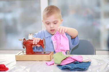 Down sendromlu bir çocuk oyuncak bebekler için elbise dikiyor, tip 21 trisonomisi olan özürlü bir çocuk, fazladan bir kromozom, özel bir çocuk..