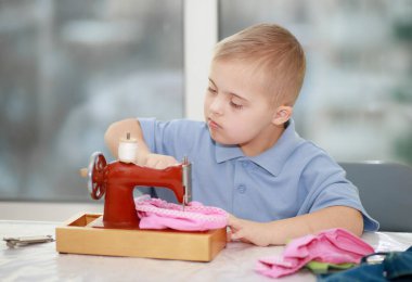 Down sendromlu bir çocuk oyuncak bebekler için elbise dikiyor, tip 21 trisonomisi olan özürlü bir çocuk, fazladan bir kromozom, özel bir çocuk..