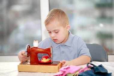 Down sendromlu bir çocuk oyuncak bebekler için elbise dikiyor, tip 21 trisonomisi olan özürlü bir çocuk, fazladan bir kromozom, özel bir çocuk..