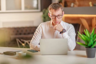 Bir iş adamı ofiste büyük bir masada dizüstü bilgisayarın önünde oturur ve internette çalışır, görüntülü konuşma, internette çalışma anları üzerine iletişim, ofisten çalışma, uzaktan çalışma kavramı..