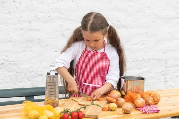 Happy little girl in an  chef costume helps to cook a pie by kneading the dough, a child smiles, cooking according to a recipe, a girl helps to cook for mom, a child\'s portrait and development.