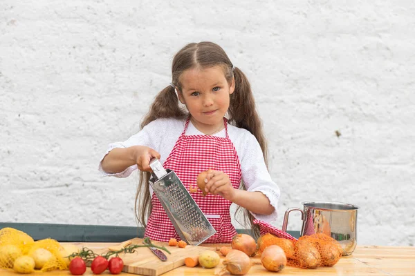 Happy little girl in an  chef costume helps to cook a pie by kneading the dough, a child smiles, cooking according to a recipe, a girl helps to cook for mom, a child's portrait and development.