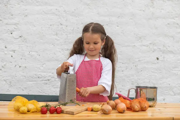 Happy little girl in an  chef costume helps to cook a pie by kneading the dough, a child smiles, cooking according to a recipe, a girl helps to cook for mom, a child\'s portrait and development.